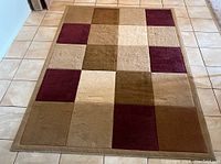 Full view of the rectangular area rug showing the square pattern in browns, beige, and burgundy.