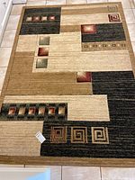 Full view top of rug showing geometric pattern and color blocks in beige, brown, black, red and green.