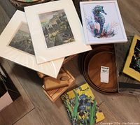 Top view of lot items including Old Quebec art prints, framed seahorse art, wooden trays, wooden boxes, Vincent address book and basket grouped on floor