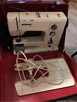 Sewing machine seated in red carrying case with foot pedal and extension table visible