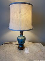 Full view of the cloisonné lamp with fabric shade on a surface, showing overall form and shade appearance.