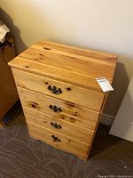 Full front view of the small wooden dresser with four drawers, showing metal handles and natural wood finish.