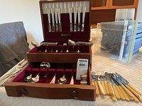 Full view of the Heritage Silversmiths flatware set in wooden case showing knives in upper section and forks, spoons, and serving pieces in lower drawer along with separate butter spreaders and additional utensils.