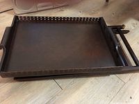 Close-up of dark metal tray with raised banked edges and cutout handles lying flat on floor.