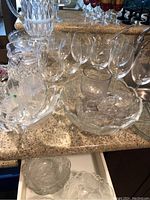 Multiple assorted clear glass pieces including wine goblets, pitchers with cut glass pattern, dessert bowls with scalloped edges, shown on countertop.