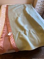 Full view of the green wool blanket with pink satin trim laid out on a bed showing size and condition.