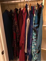 Multiple ladies dresses hanging in a closet, showing variety of colors and patterns.