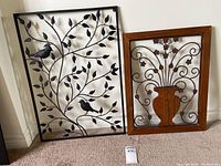 Pair of nature-themed wall art pieces leaning against a wall, showing the full view of both metal and wood elements.