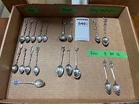Complete assortment of 17 miniature spoons arranged in a cardboard box, with some labeled areas for stamps and origin notes.