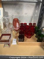 Overview photo showing assortment of cranberry glassware in red and green, clear glass decanter, pitcher, and small dishes.
