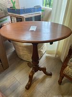 Full view of oval wooden side table with single pedestal base and curved feet.