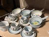 Photo showing all items in the lot including cups, saucers, bowls, and creamer arranged on cardboard with visible tags.