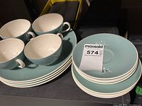 Full view of stacked large plates, side plates, cups and saucers in muted teal-blue with floral accents