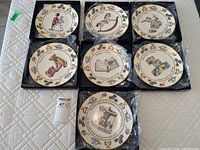 Top view of the seven individual boxed Royal Worcester plates, each plate decorated with day of the week themed illustrations and borders with toys.