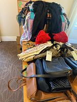 Photo showing various scarves piled on chairs and multiple hats, with several bags and purses laid out on table
