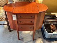 Wooden sewing cabinet front view showing three drawers and octagonal side compartments closed.