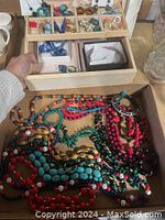 Overview photo of several colorful bead necklaces laid out inside an open wooden jewelry box drawer.