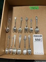 Full view of the set of 11 sterling silver souvenir spoons laid out in a box, showing variety in handle designs and enamel decoration.