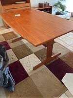 View of teak dining table assembled with rectangular top and pedestal base on multicolor rug.