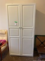 Front exterior view of the white wardrobe cabinet showing paneled double doors with round knobs.