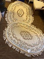 Two oval wool rugs laid out on floor, showing overall size, design, and fringed edges