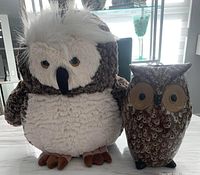 Photo showing a white and brown plush owl stuffed animal next to a brown ceramic owl vase with detailed eyes and feathers on a countertop.