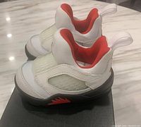 Pair of baby-sized Nike Jordan 5 Retro Little Flex TD sneakers in white, university red, and black colors shown on top of original shoebox.