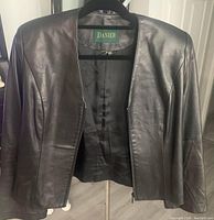 Front view of black leather jacket on a hanger with zipper partially open showing inner lining and Danier label.
