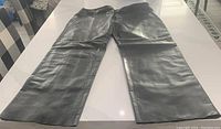 Full view of the black leather slacks laid flat showing overall condition and shape.