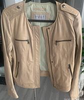 Front view of cream leather jacket by Andrew Marc showing zipper closure, pockets, and snap button shoulder epaulettes.