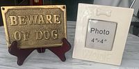 Photo showing solid brass Beware of Dog plaque on dark brown stand and ivory ceramic Woof photo frame side by side