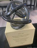 Photo showing the Endless Knot glass sculpture on its box with text describing its symbolism of never-ending connections and harmony.