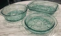 Set of three green glass ovenproof dishes on marble counter, showing embossed textured patterns and thick glass construction.