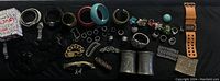 Wide shot of bracelets, rings, arm cuffs, earrings, and watches arranged on black cloth.