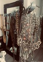 Photo of assortment of costume jewelry necklaces hung on a metal organizer with various styles and colors visible including pearl strands, gold-tone chains, and beaded necklaces.
