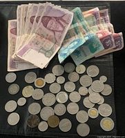 Overview of South Korean won banknotes along with a wide variety of international coins spread out on a black surface.