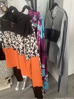 Three brand new women's activewear pantsuits size XL hanging on black hangers. One set is black, white, and orange with animal print, one is purple/blue/white tie-dye, and one is gray with black and white checkered accents.