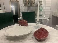 Display of the Beauceware leaf dish, red art pottery vase, ivory bowl, and glass candlestick on a marble table with dining chairs and mirror in the background.