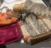 Six assorted women's purses laid on a table showing variety of colors, materials and sizes