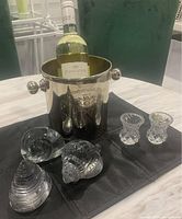 Photo showing one champagne bucket holding a bottle of wine with five clear glass decorative items placed on a black cloth.