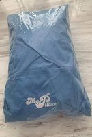 Front view of the blue My Pillow travel pillow inside plastic packaging, showing brand logo.