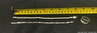 Photo shows two sterling silver bracelets and one ring laid against a black background with a yellow measuring tape showing lengths of bracelets and ring size