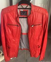 Front view of red leather jacket open on a hanger showing striped inner lining and zipper pockets.