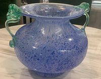 Front view of a large blue speckled art glass vase with green curved decorative handles, flared rim and rounded shape.