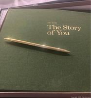 Green hardcover journal titled 'The Story of You' with gold pen lying on cover.
