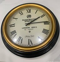 Front view showing full clock face, black outer frame with gold bezel, and Roman numerals.