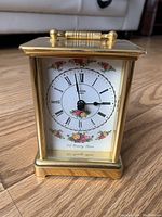Front view of brass clock showing floral decorated white clock face with black Roman numerals and Bulova branding.