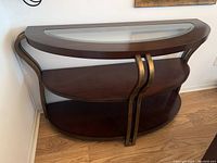 Front view of the console table showing glass inset top, bronze metal frame, dark brown wood shelves.