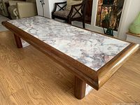 Full view of the large custom coffee table with pink/grey granite inserted into a solid wood frame and four solid wood legs on a hardwood floor.