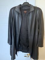 Front view of black leather coat hanging on Danier branded hanger, showing open front and inner lining.